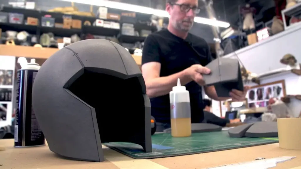 costume helmet sitting on table, person in background working on costume